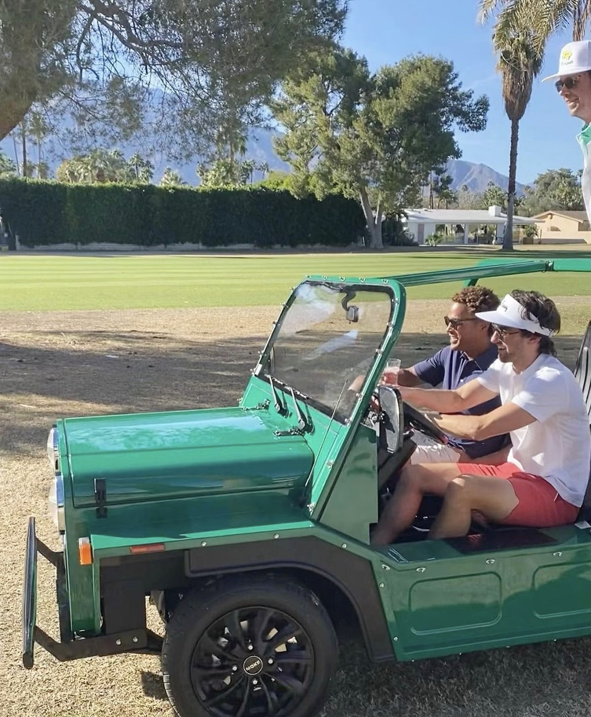 Two people in a green Moke beside a desert golf course