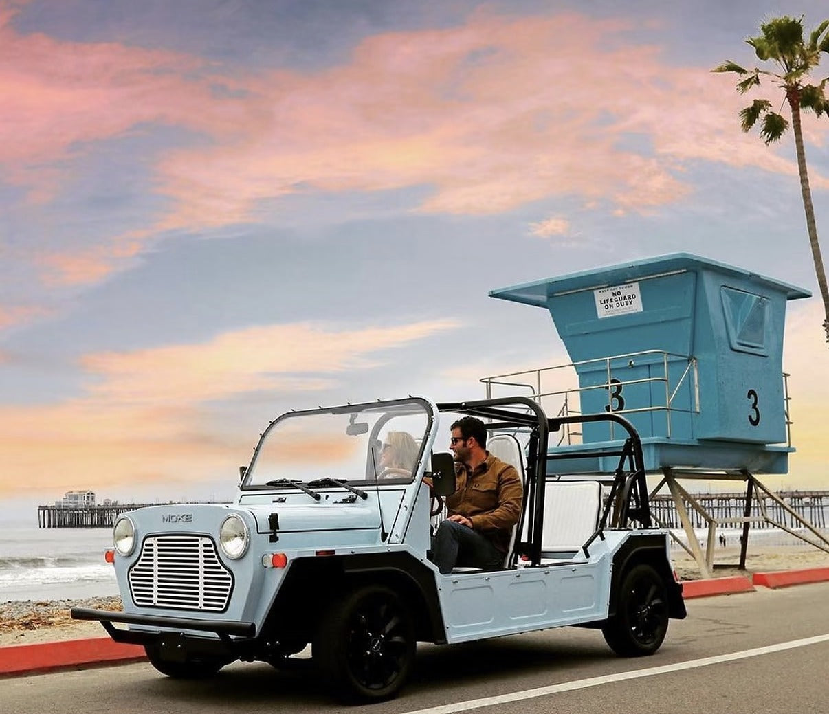 A white Moke parked by a lifeguard tower on a California beach at sunset