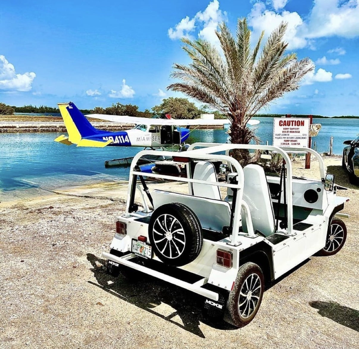 A white Moke parked by the water in Key West with a seaplane behind it