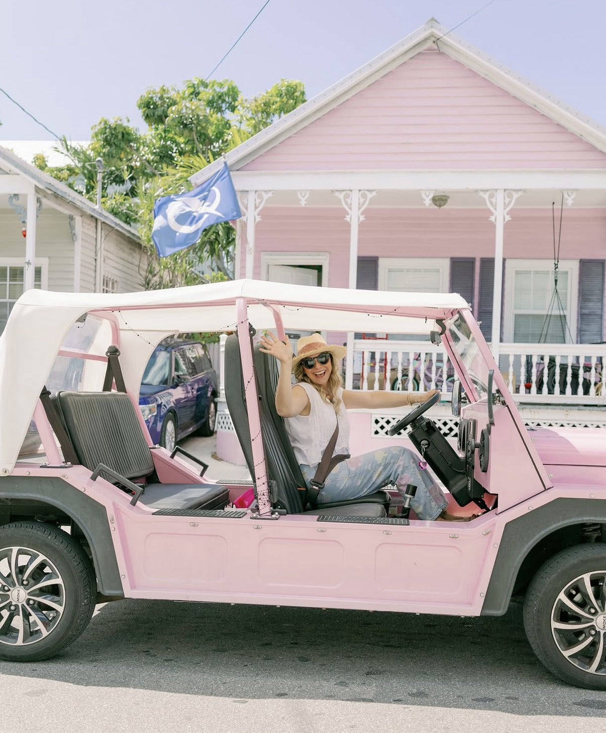 A woman seated in a pink Moke outside a pastel Key West cottage
