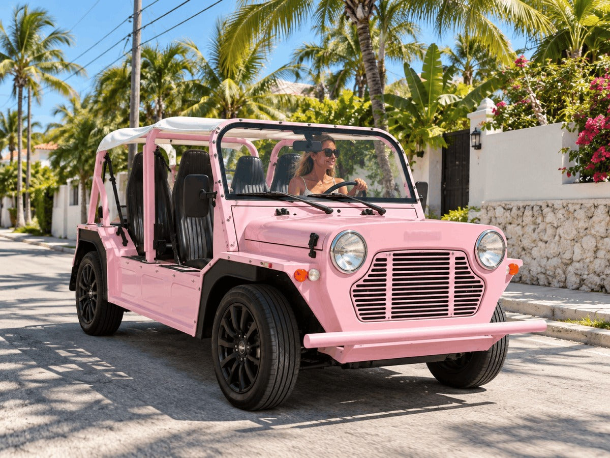 A woman driving a pink Moke down a residential street lined with palms