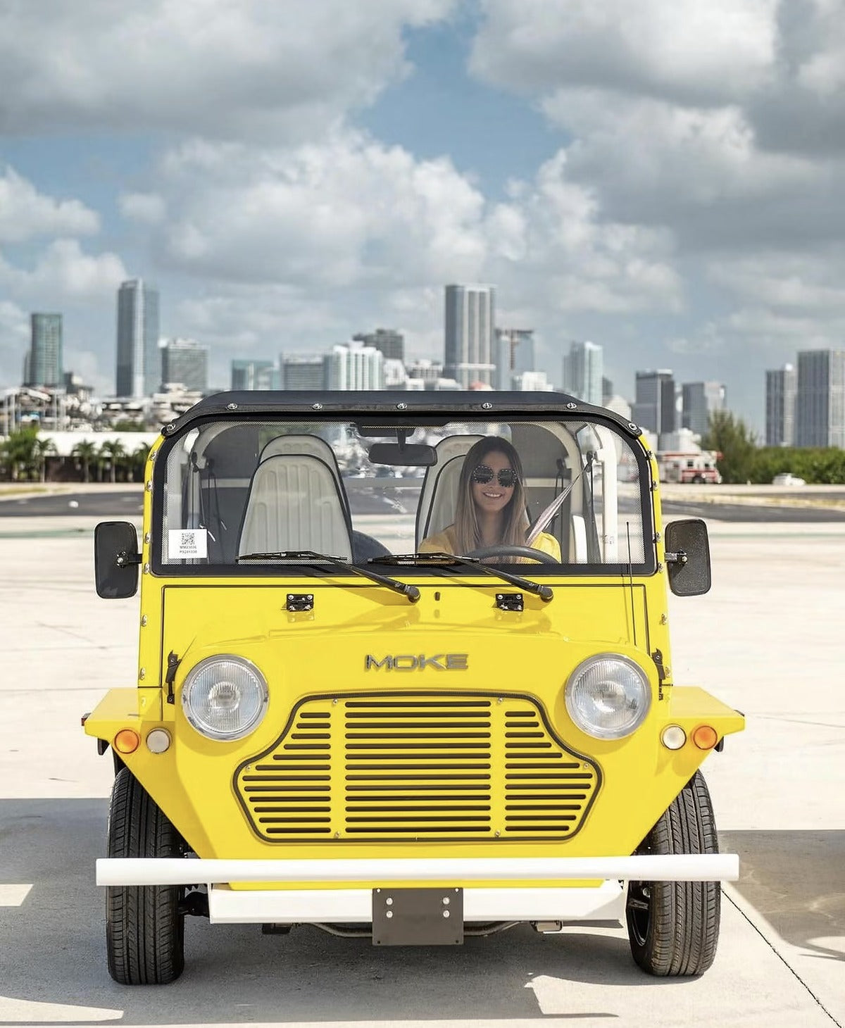 A yellow Moke parked with the Miami skyline behind it
