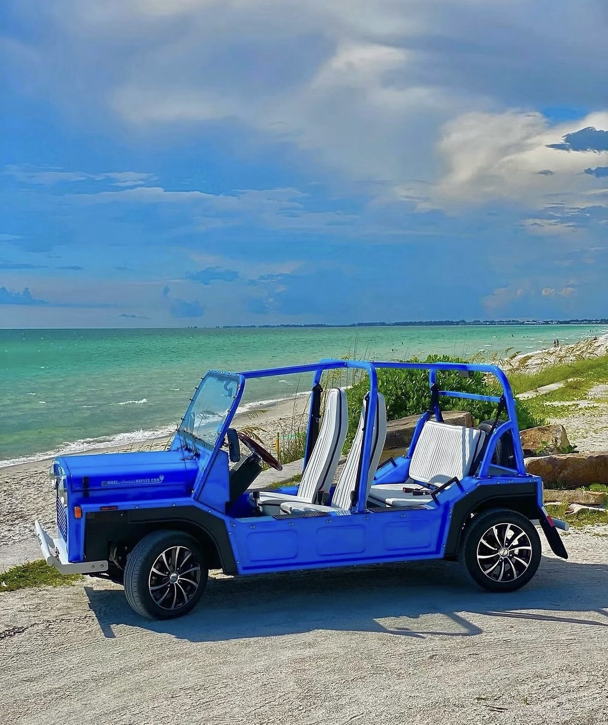 A blue Moke parked beside the water under a wide Florida sky